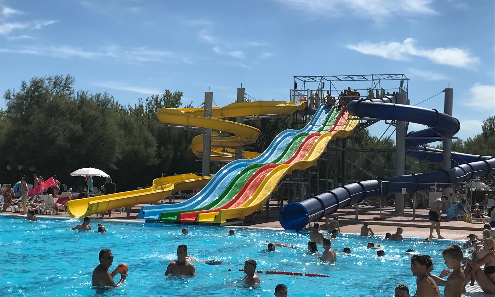 Waterpark with colorful slides, people swimming and playing in a bright, sunny area with trees in the background at Isamar