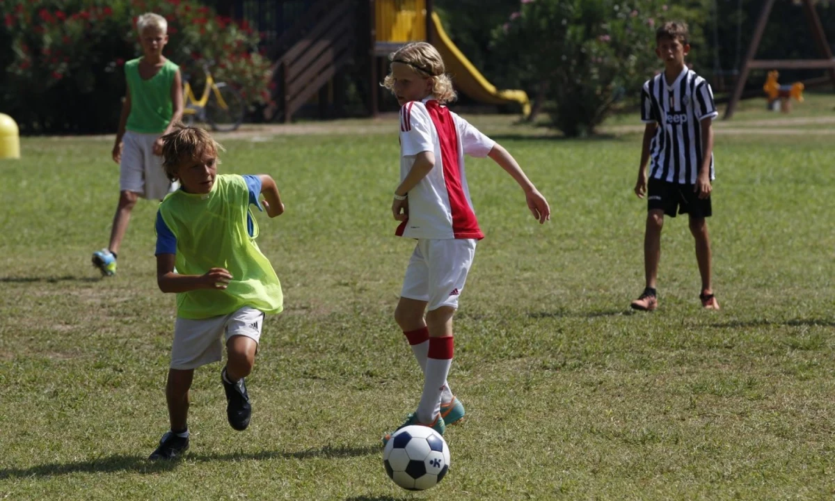 Children playing soccer on grassy field, with playground equipment in the background at Isamar