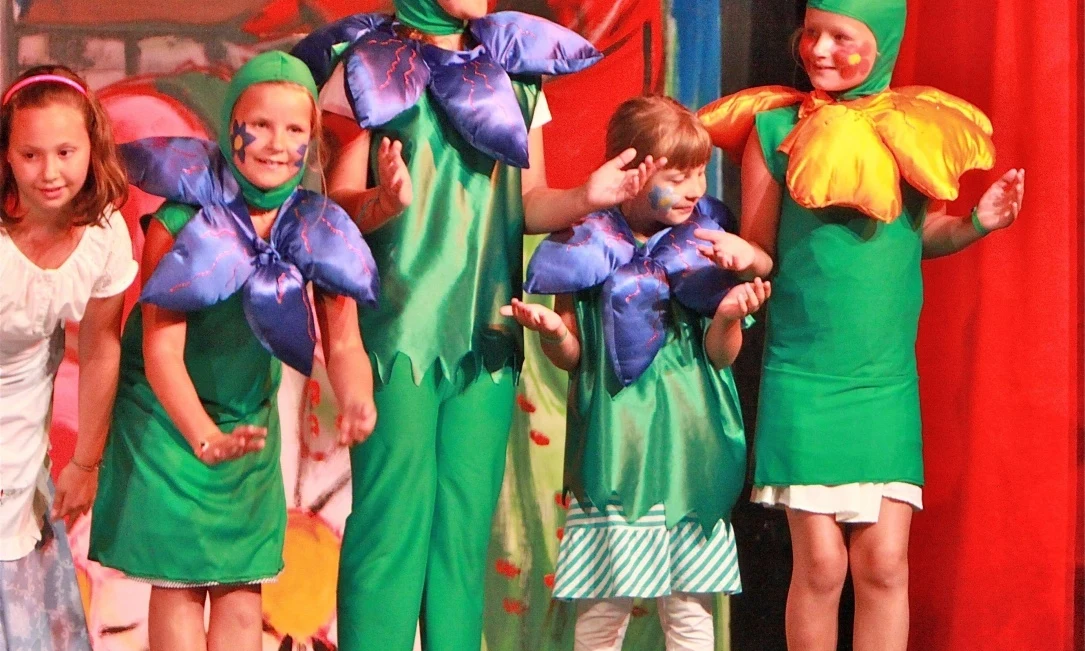 Children wearing flower costumes on stage during a performance, with a painted backdrop at Isamar