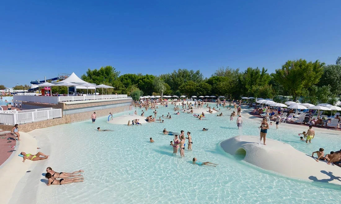 People swimming and sunbathing in a pool surrounded by trees and lounge chairs at Isamar