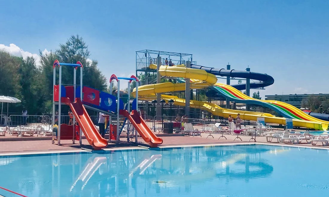 Children's water playground featuring colorful slides, adjacent to a swimming pool with loungers and larger water slides in the background at Isamar