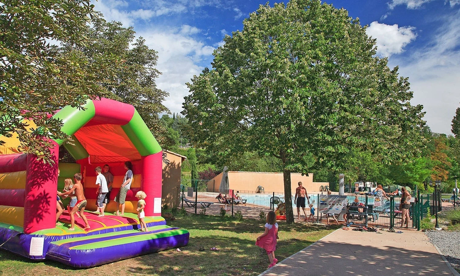 Children jumping on a colorful bouncy house near a pool area with adults relaxing nearby at Ardeche Camping 