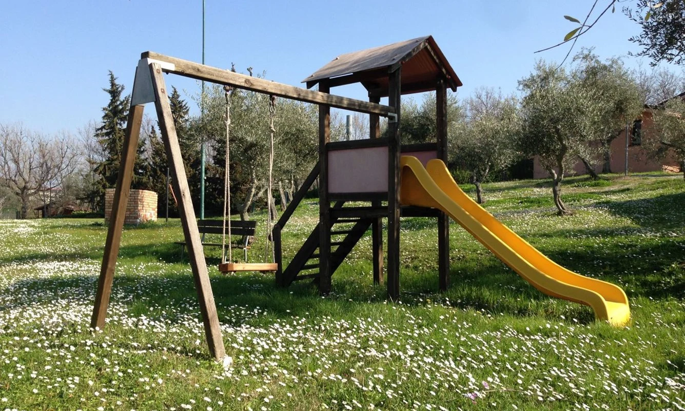 Playground set with a swing and yellow slide, situated on a grassy field dotted with white flowers at Centro Vacanze San Marino