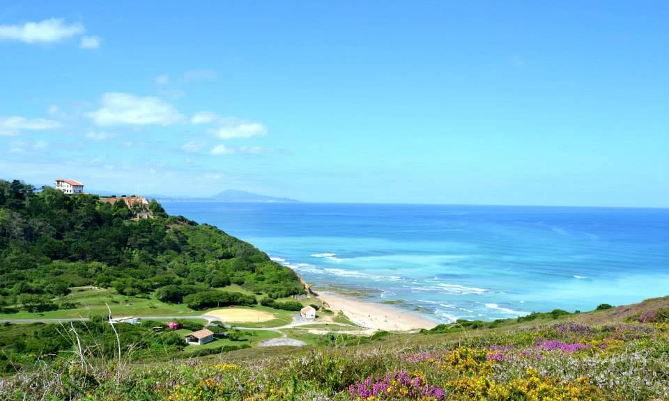 Ocean waves gently meeting a sandy shore, surrounded by lush green hills and distant mountain view at Ur-Onéa