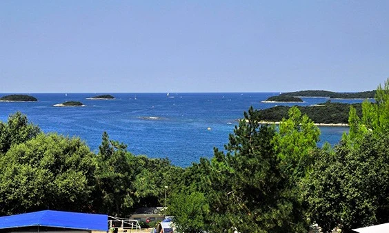 Campsites and caravans overlooking a dense forest and coastal view with blue sea and small islands under a clear sky at Orsera