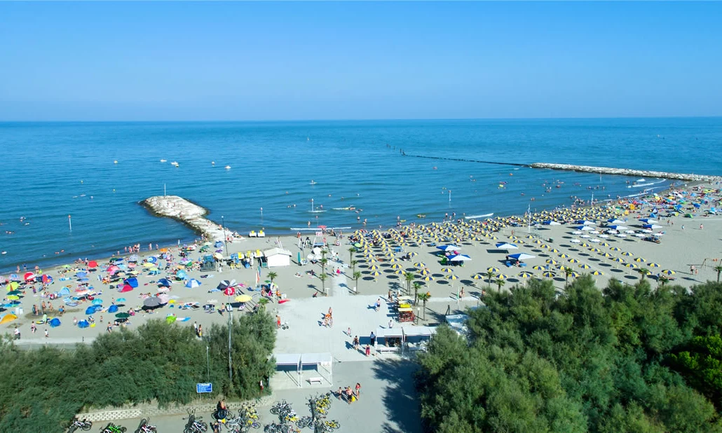 Beachgoers are sunbathing and swimming on a crowded beachfront, featuring colorful umbrellas and a clear blue sea backdrop at Isamar