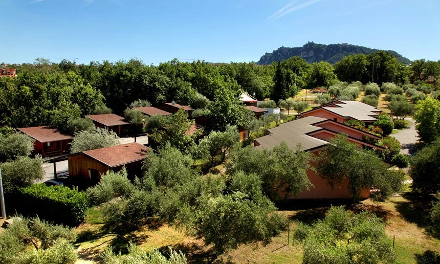 Wooden cabins situated among trees and greenery, with a mountain visible in the distance at Centro Vacanze San Marino