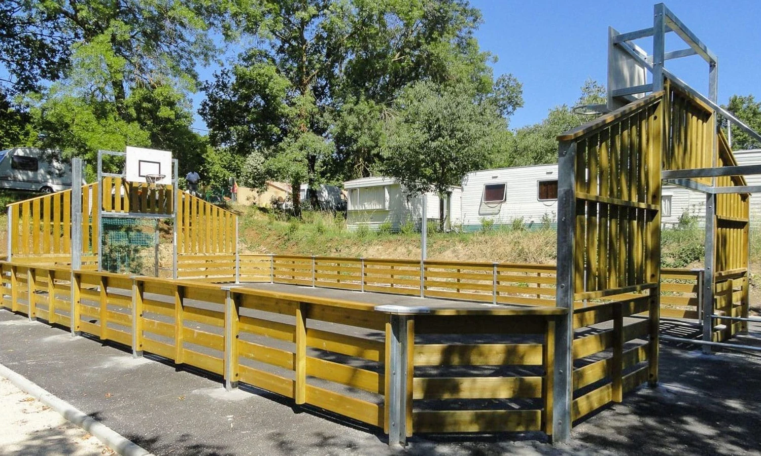 Wooden sports court with basketball hoops surrounded by caravans and trees at Ardeche Camping 