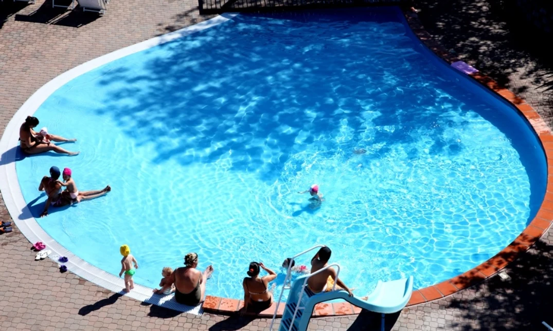 Swimming pool with children and adults relaxing, playing, and using slide; surrounded by sun loungers on paved area at Centro Vacanze San Marino