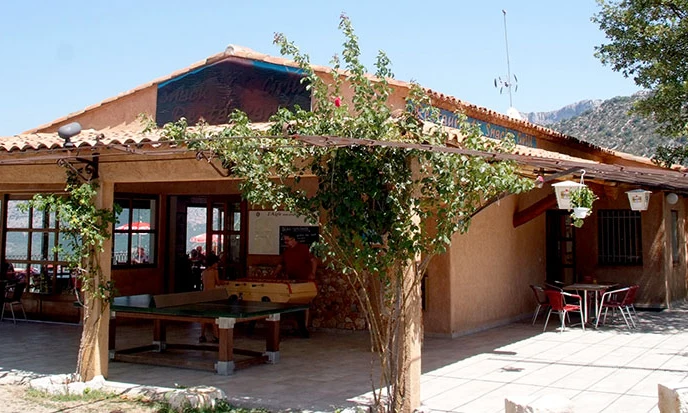 Building with covered patio housing table games, vine-covered pergola, surrounded by trees and mountains on a sunny day at de l'Aigle