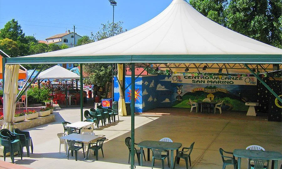 Several tables and chairs under a large canopy in an outdoor recreational area with colorful murals at Centro Vacanze San Marino