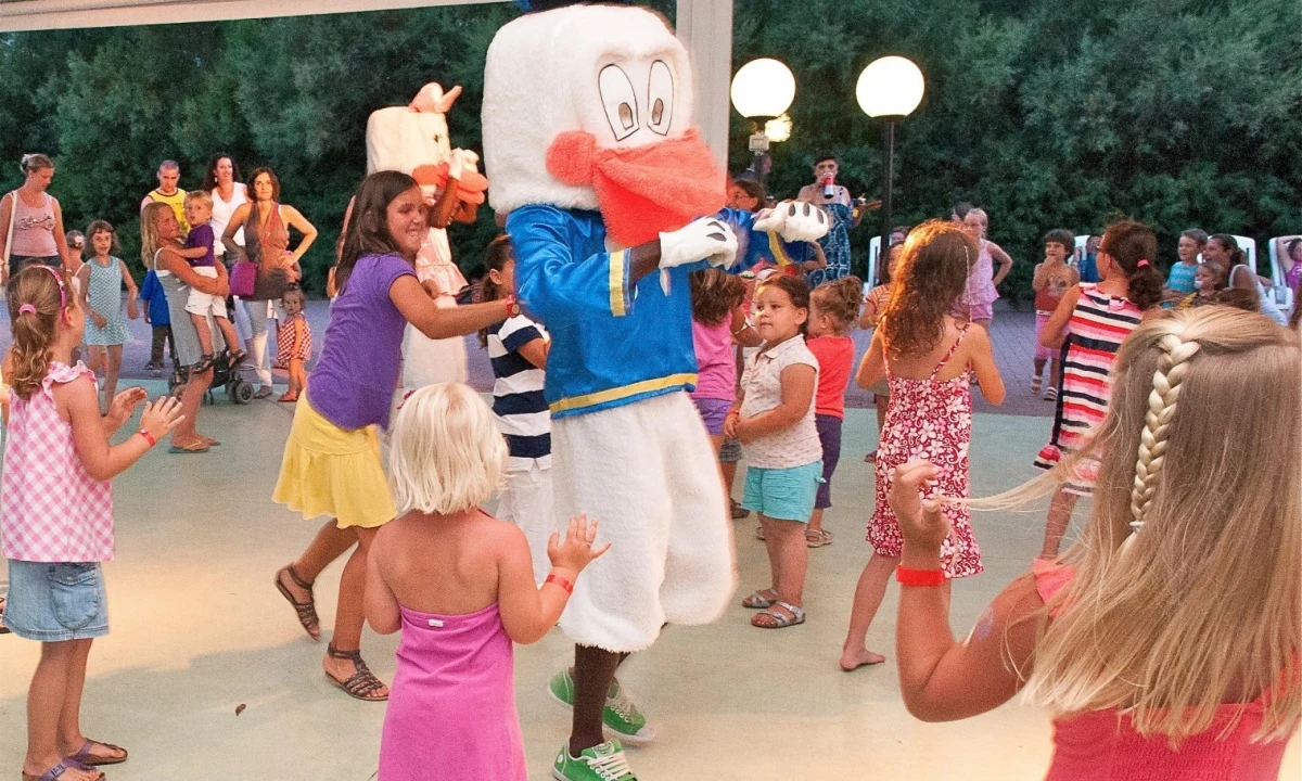 Mascot duck dancing with children in outdoor gathering area at Isamar