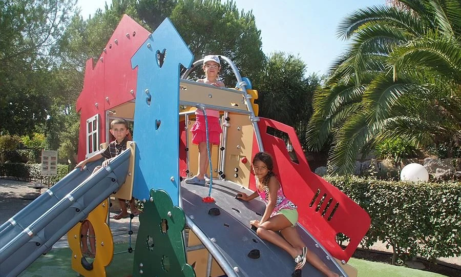 Children climb and play on a colorful playground structure surrounded by greenery and palm trees at Leï Suves