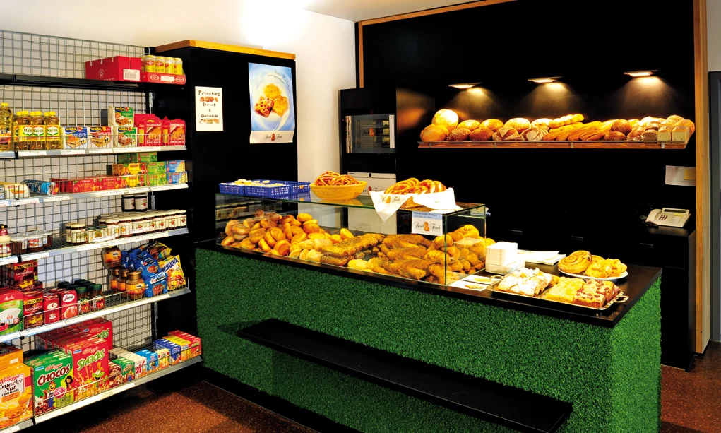 Bakery counter displaying fresh bread and pastries; shelves with groceries line the wall; warm lighting above at Natterer See