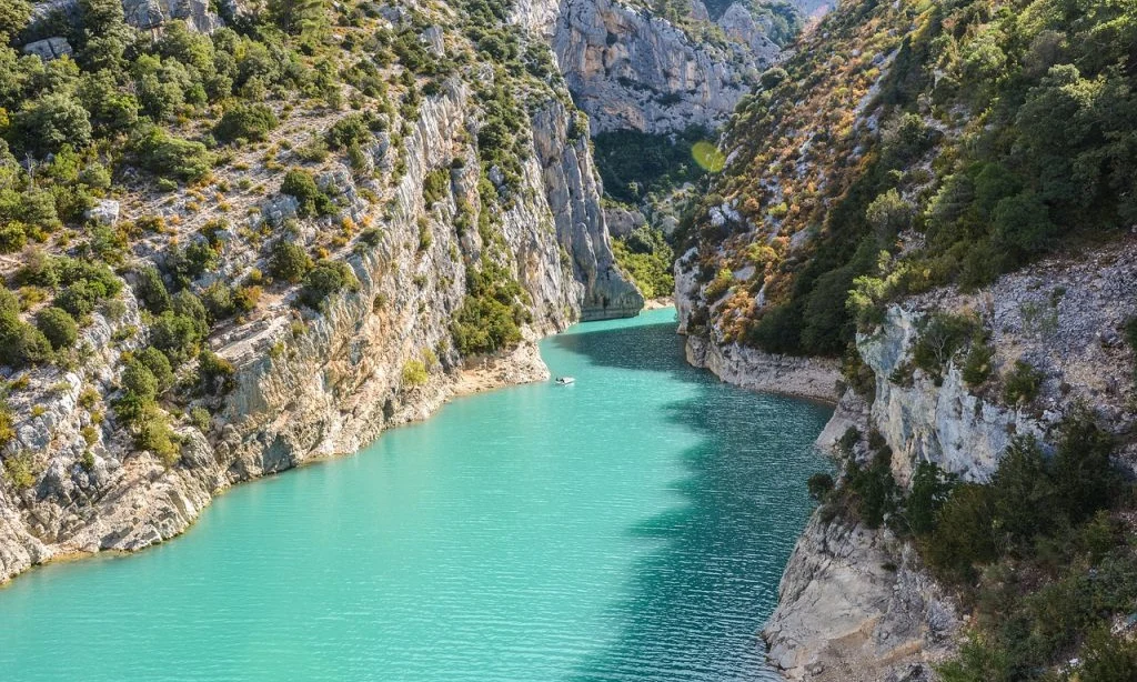 Turquoise river flowing between steep, rocky cliffs covered in lush greenery at de l'Aigle