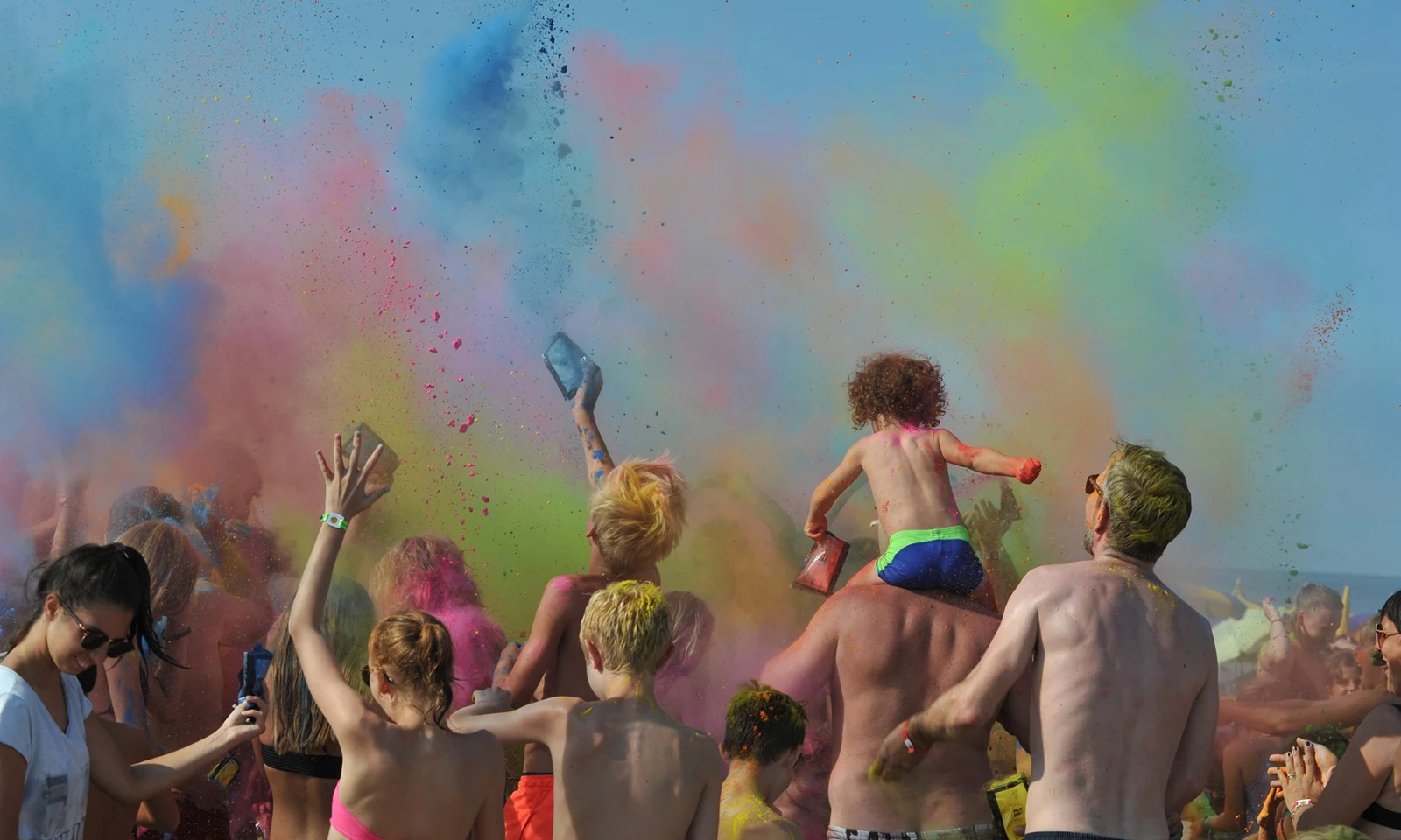 People tossing colorful powder up into the air at an outdoor festival at Isamar