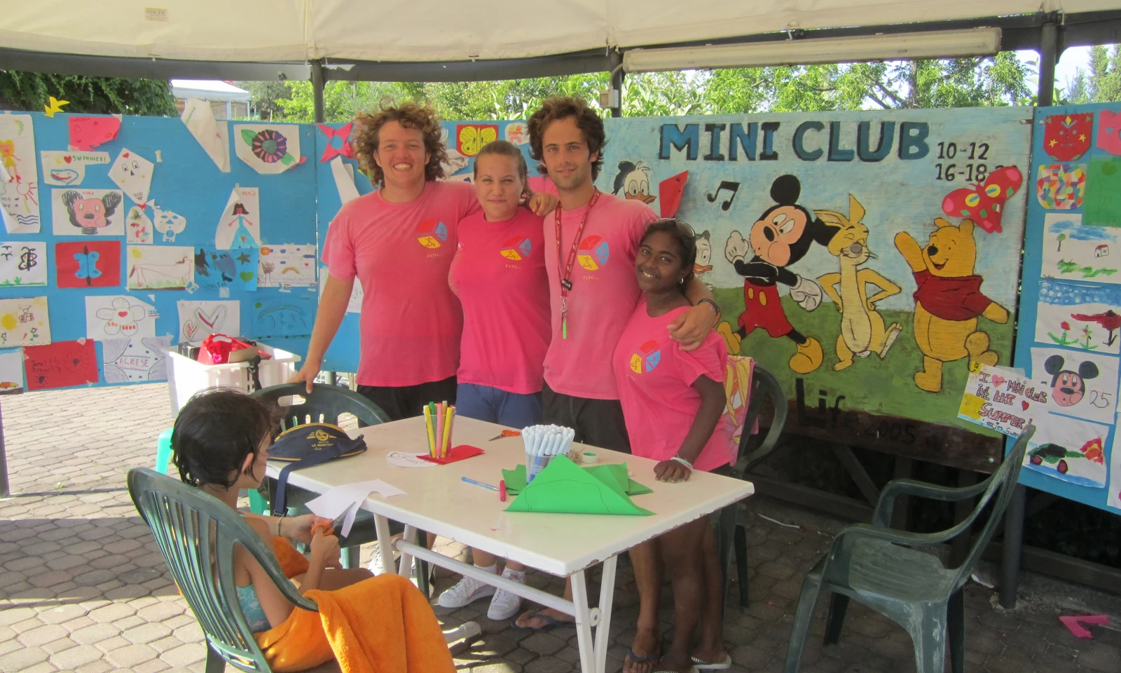 Four people pose beside a table with art supplies, a young child sits and crafts at Centro Vacanze San Marino