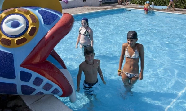 Children playing in a swimming pool near a large decorative fish fountain at Oasi