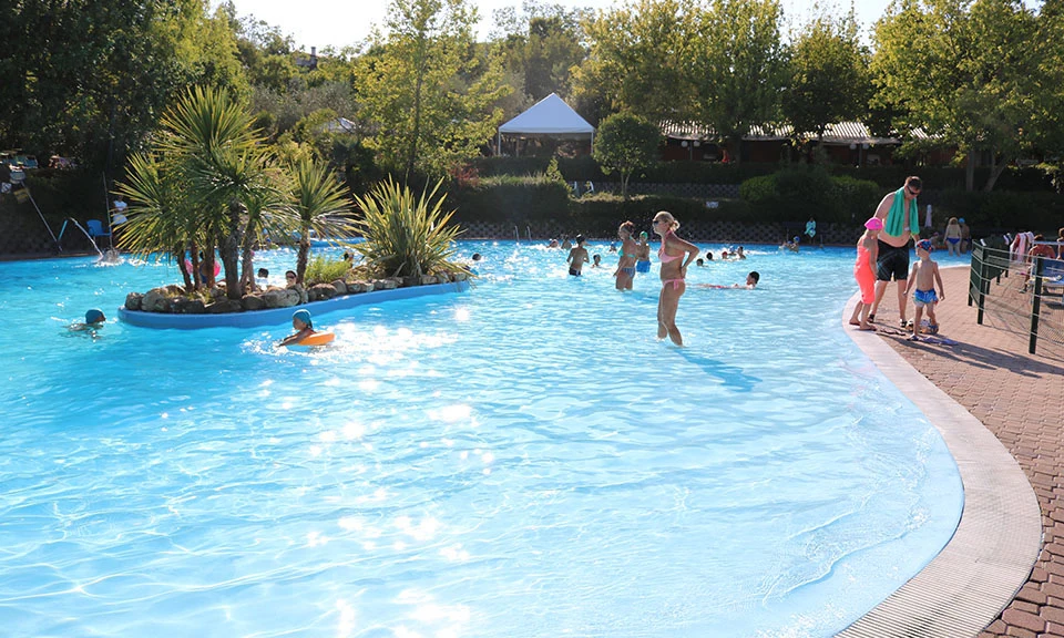 Swimmers enjoy a large outdoor pool surrounded by trees and a tiled deck at Centro Vacanze San Marino