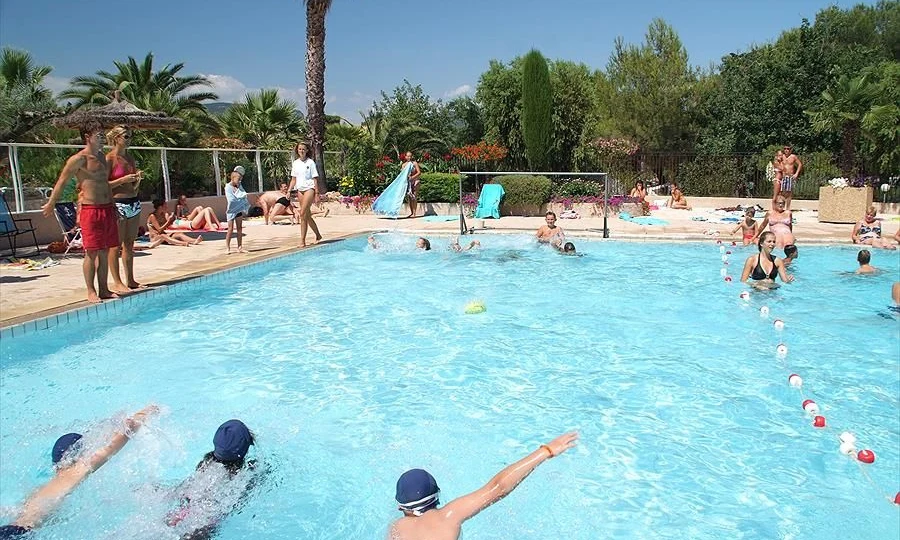 Swimmers practicing in a lively outdoor pool area with onlookers and lush greenery in the background at Leï Suves