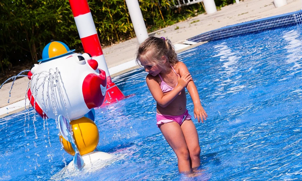 Young girl plays in a splash pool with a water fountain statue at Les Amiaux