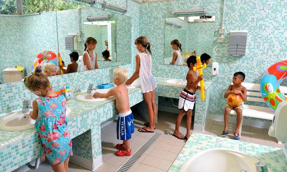 Children washing hands and playing with toys in a tiled bathroom with mirrors at Isamar