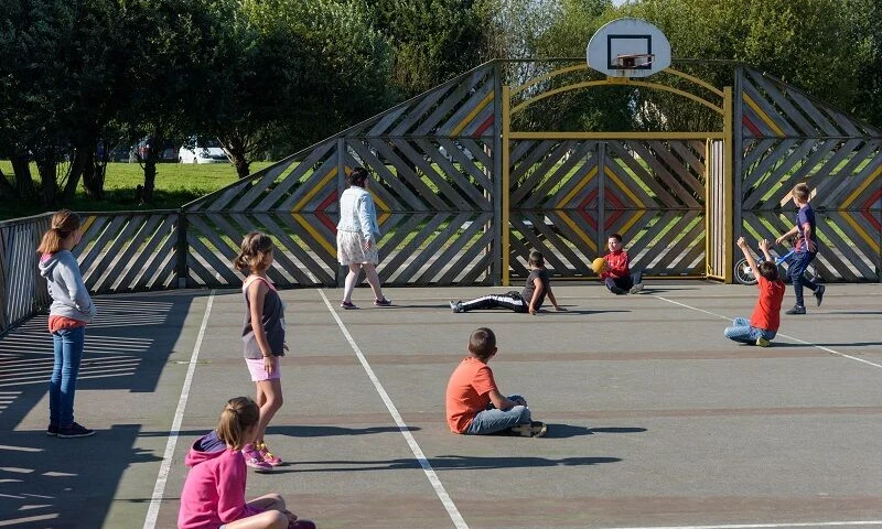 Children play together on a fenced basketball court surrounded by trees at Domaine de Mesqueau