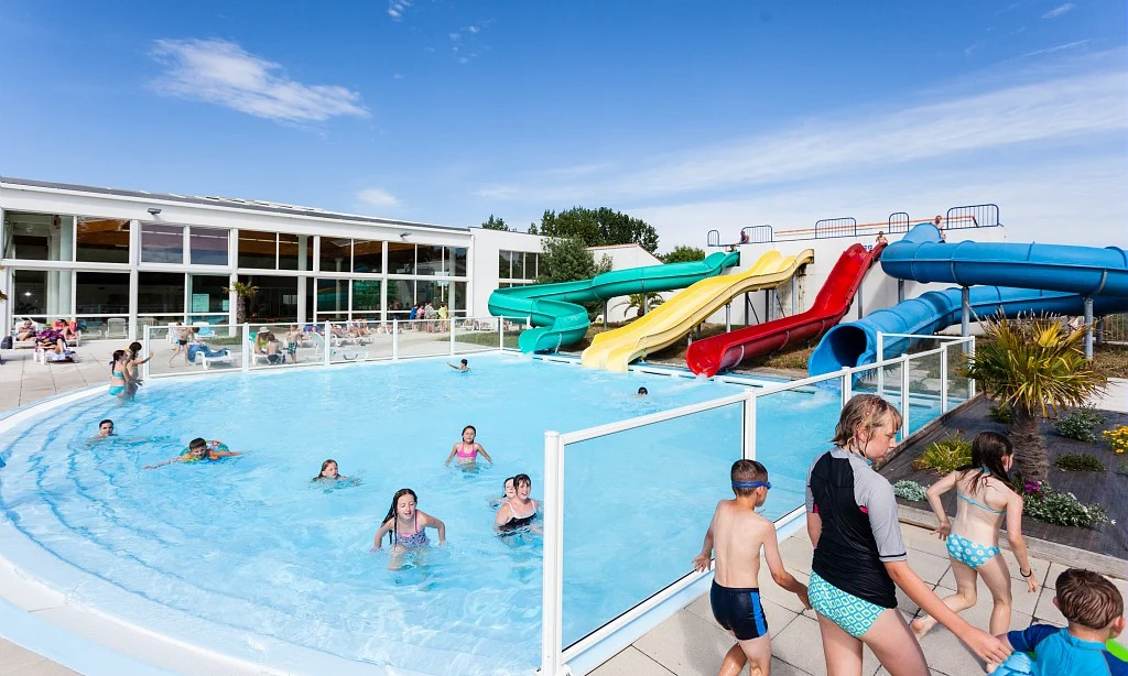 Children swimming and playing in an outdoor pool with colorful water slides and a glass-walled building nearby at Les Amiaux