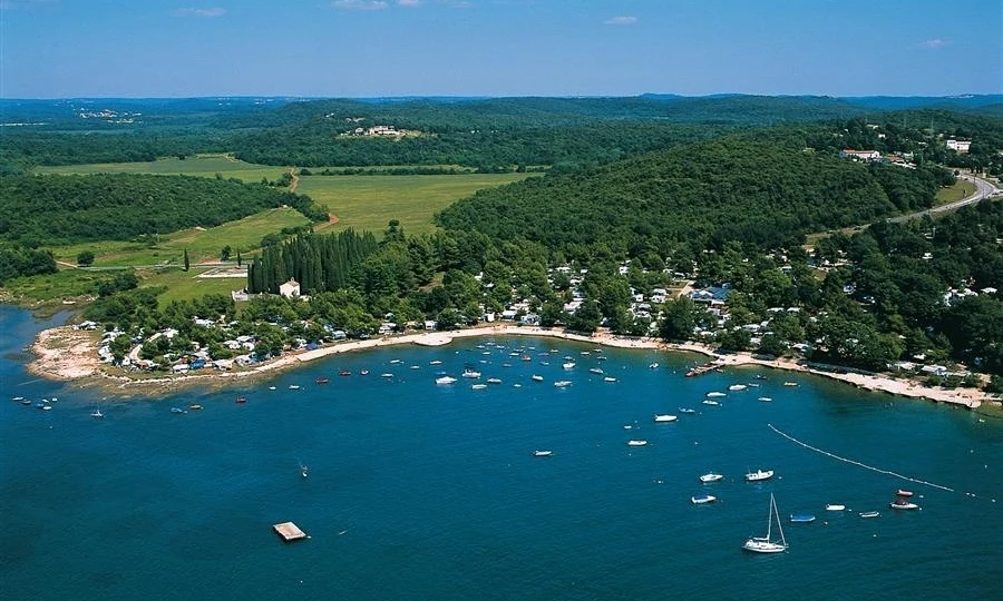 Boats floating in a calm bay, adjacent to a tree-covered shoreline with scattered buildings at Orsera