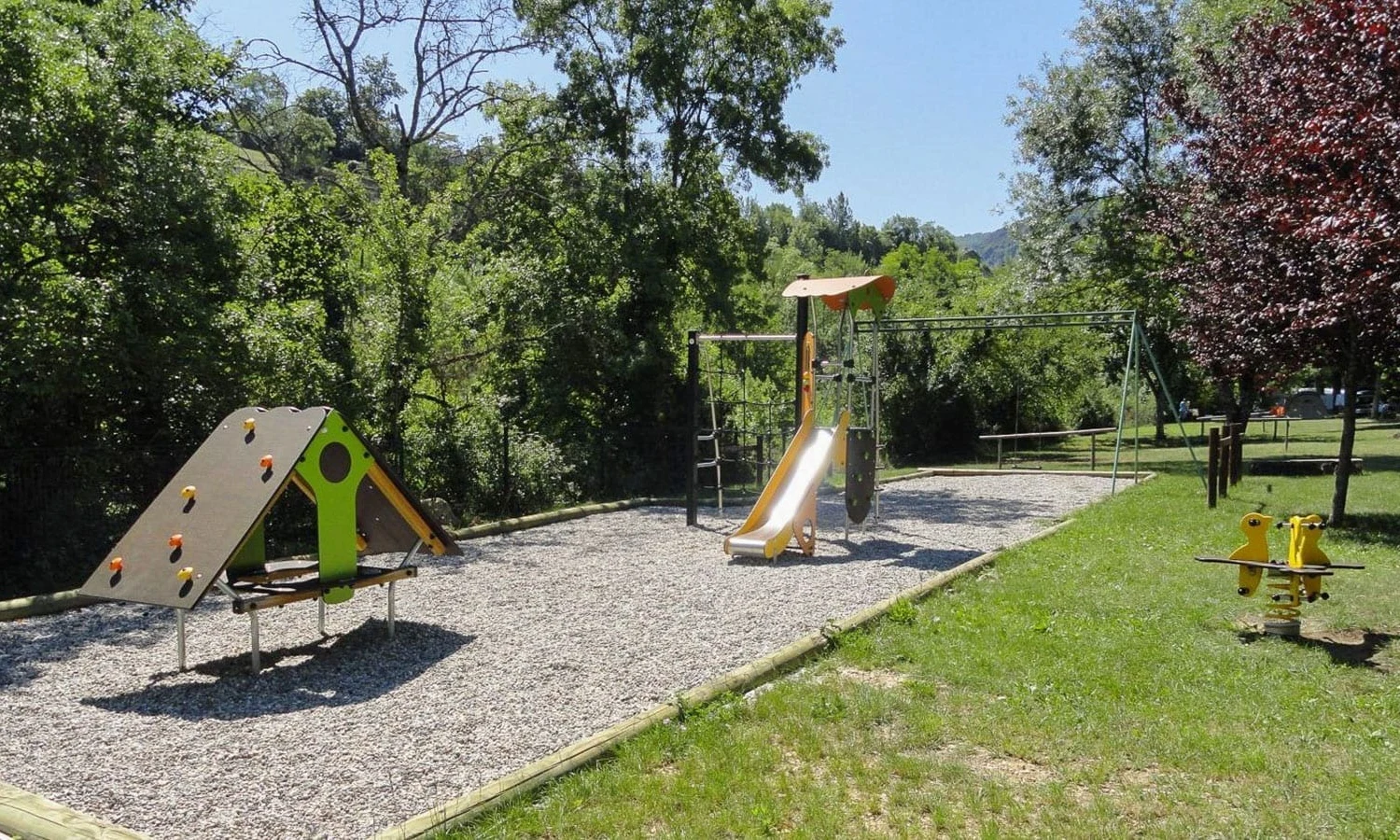 Playground features a climbing structure, a slide, and a seesaw amidst trees and green grass at Ardeche Camping 