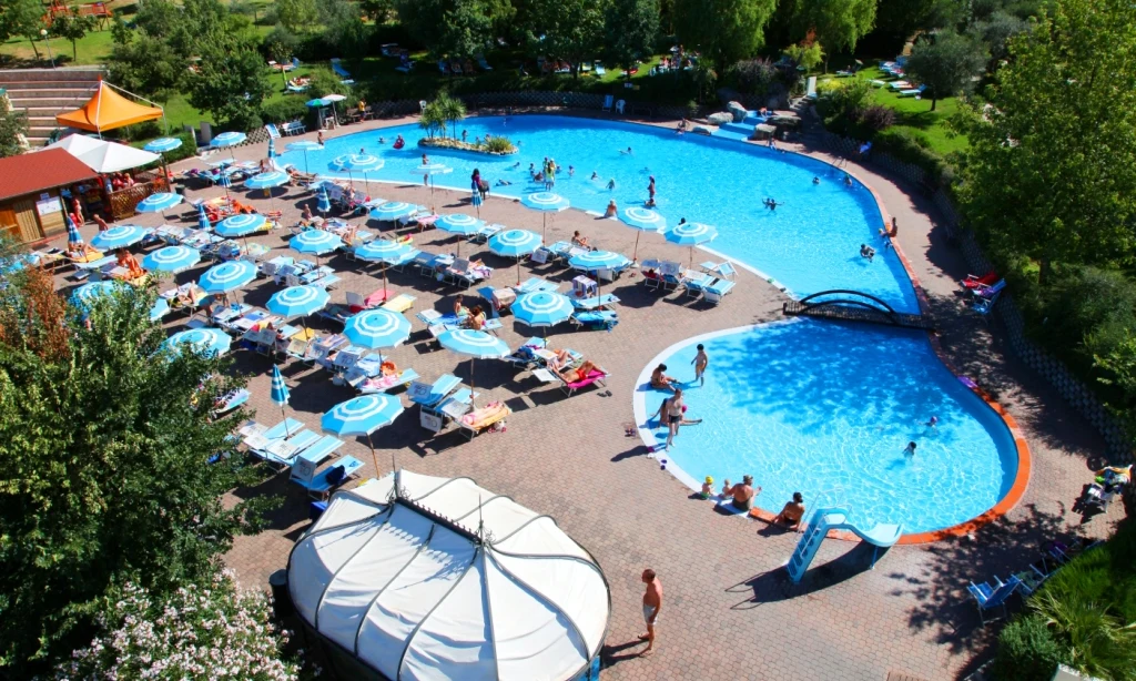 People swimming and sunbathing near large pools and loungers, surrounded by lush greenery at Centro Vacanze San Marino