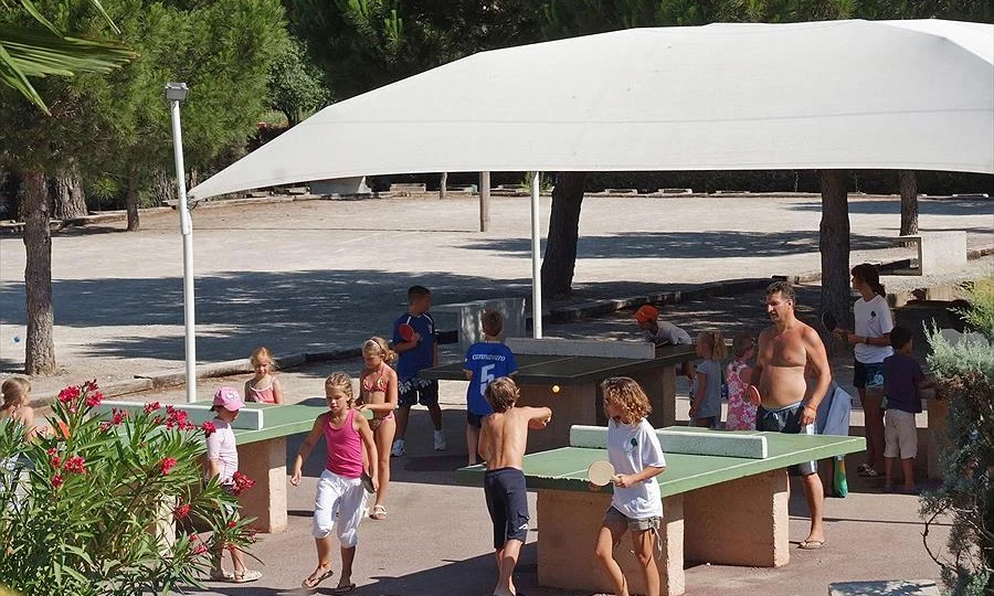 Children playing table tennis under a shade canopy amidst trees and concrete paths at Leï Suves