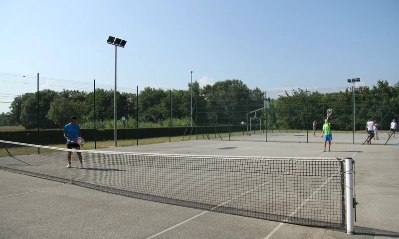 People are playing tennis on an outdoor court surrounded by a high fence and greenery at Leï Suves