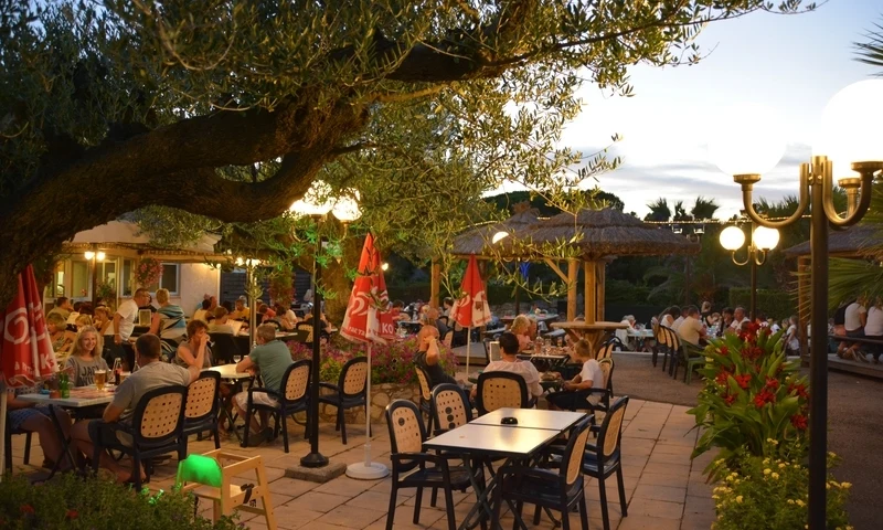 People dining at outdoor tables under trees and umbrellas at Leï Suves