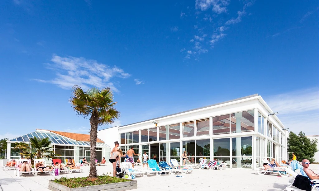 People relaxing on sun loungers outside a modern building with large windows under a clear blue sky at Les Amiaux