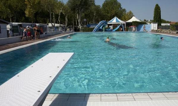 Swimming pool with diving board, people swimming and relaxing, surrounded by trees and tents at Oasi