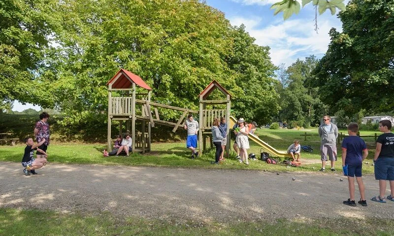 Wooden playground with slides and climbing structures, surrounded by adults and children in a grassy park at Domaine de Mesqueau