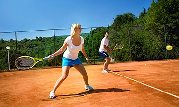 Two people playing tennis on a clay court surrounded by trees at Orsera