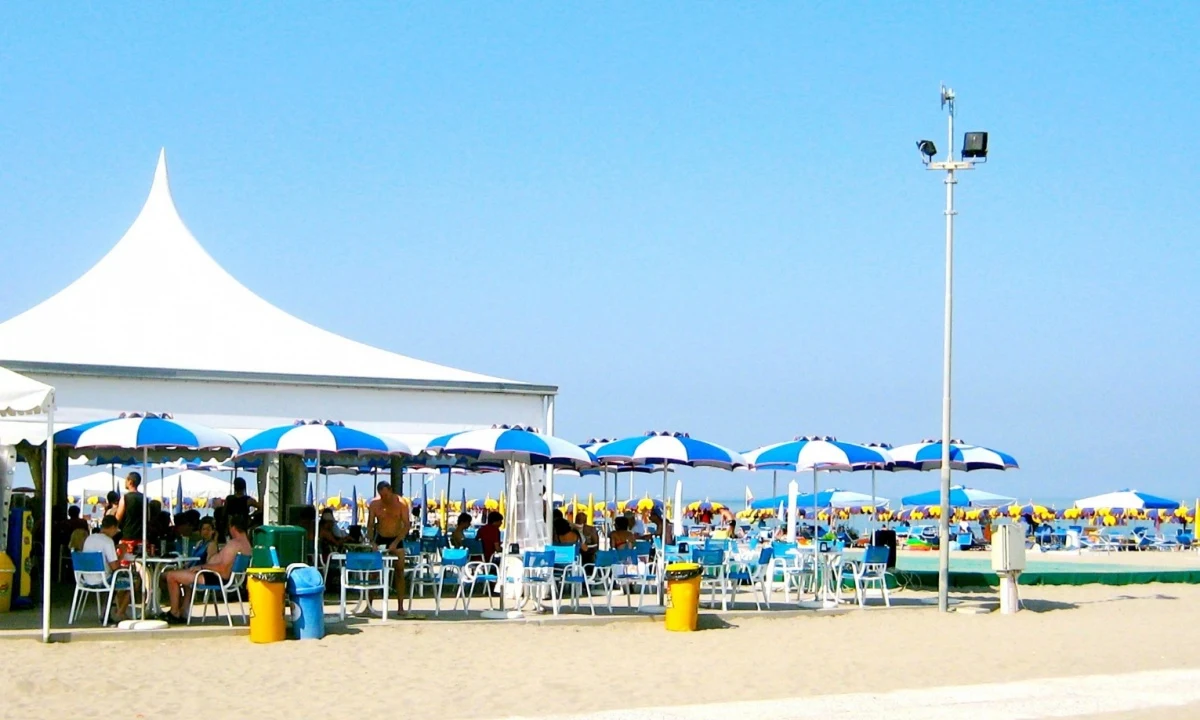 White canopy sheltering people sitting and relaxing under blue-striped umbrellas on a sunny beach at Isamar