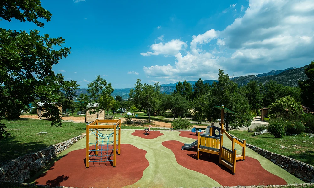 Playground equipment in use set on a colorful soft surface, surrounded by trees and mountains at de l'Aigle