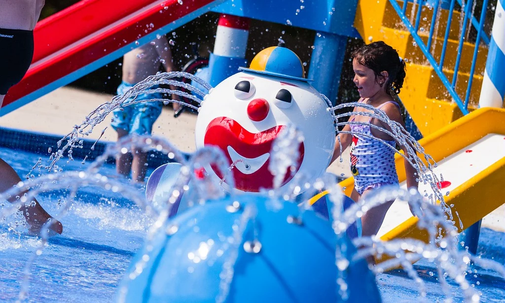 Children playing in a colorful water park, interacting with spraying fountains and slides on a sunny day at Les Amiaux