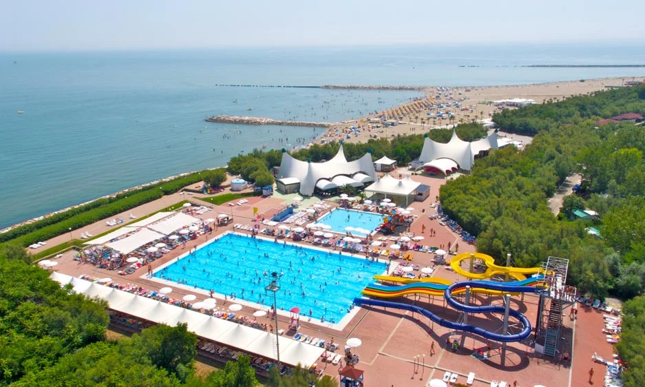 Aerial view of a swimming pool with waterslides surrounded by people, near a beach and greenery at Isamar