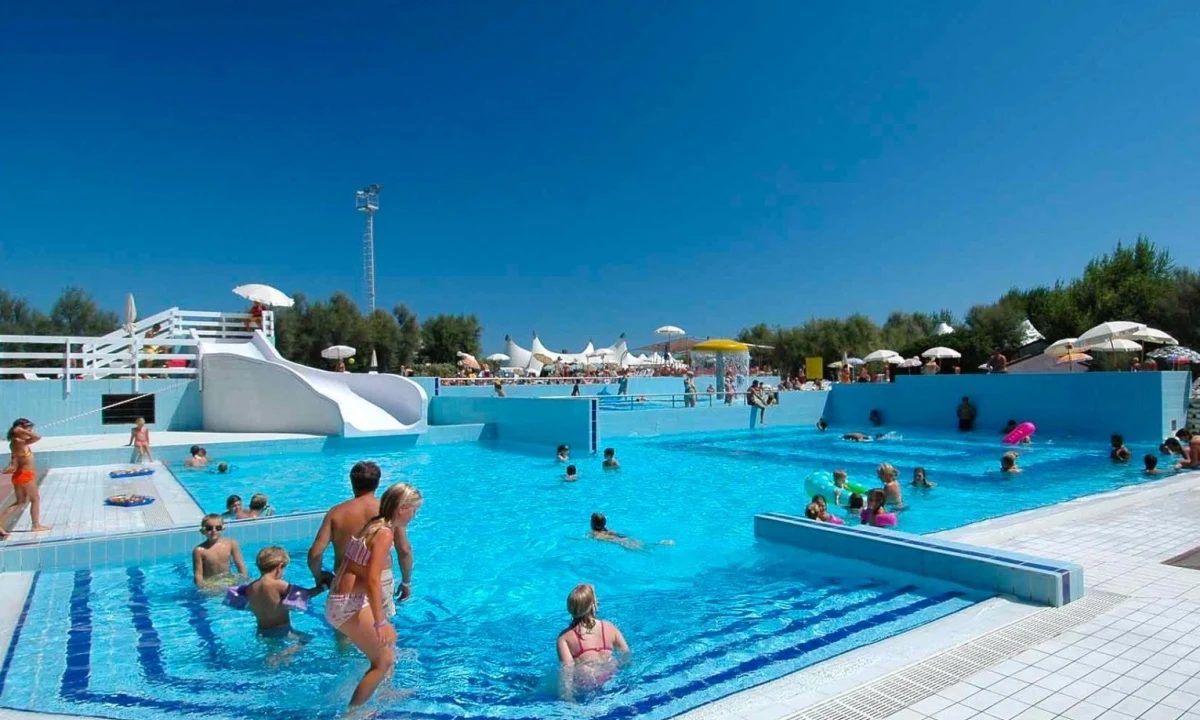 People swimming and playing in a large outdoor pool with slides and surrounding umbrellas at Isamar