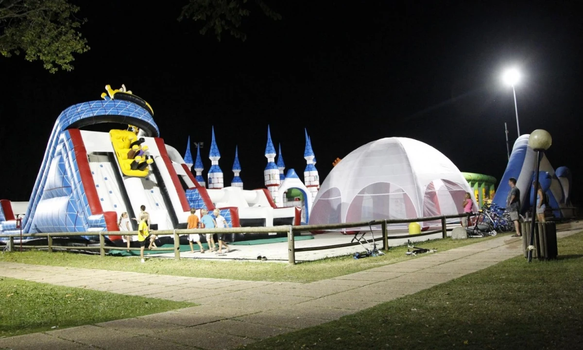 Large inflatable play structures, including a slide and castle, surrounded by children playing and adults watching at Isamar