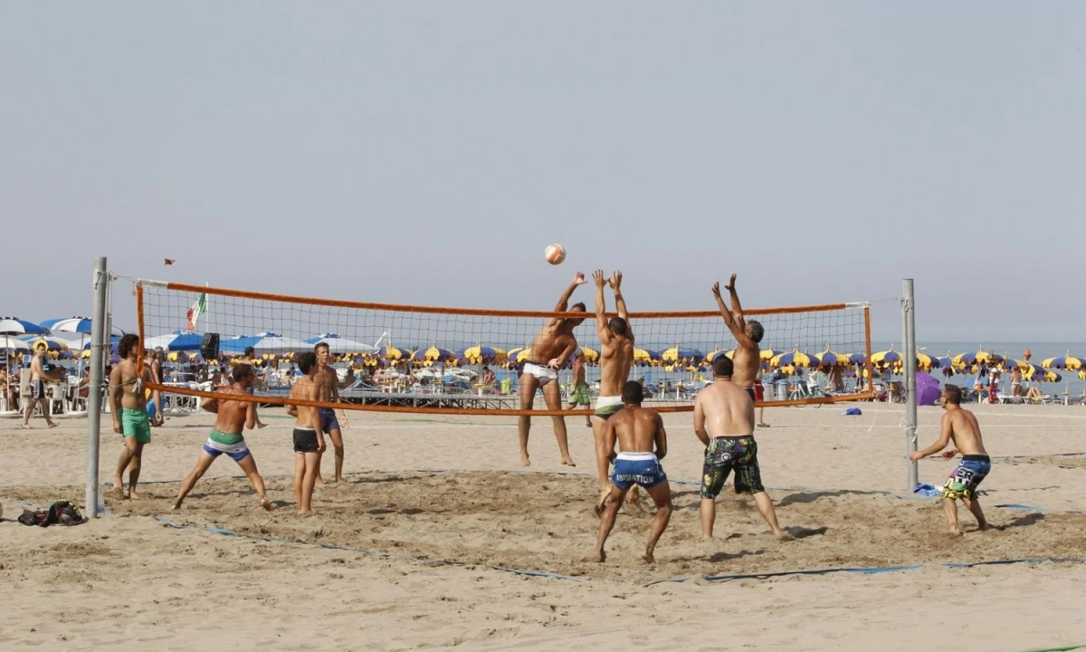 People playing beach volleyball, jumping to hit the ball over the net, surrounded by sunbathers and beach umbrellas at Isamar