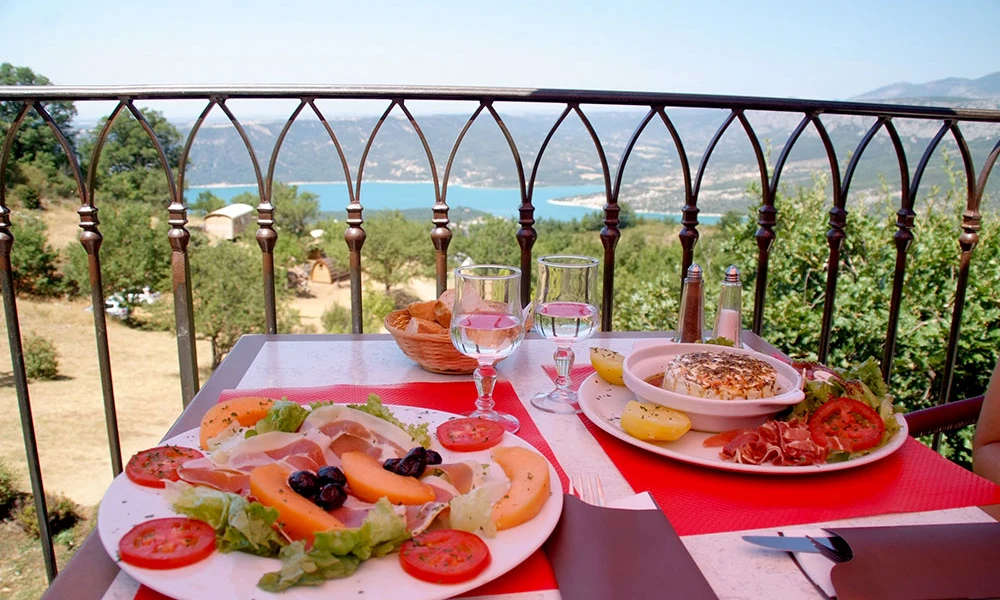 Lunch plates with salads and meat on a table, overlooking a scenic mountain lake view with trees at de l'Aigle