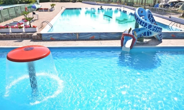 Children splashing in a pool with a slide and fountain; another larger pool in the background at Oasi