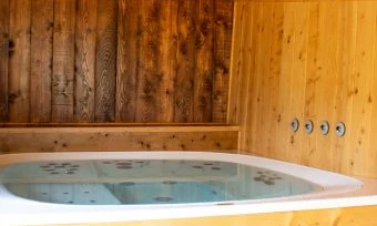 A hot tub filled with water is situated inside a wooden cabin at de l'Aigle