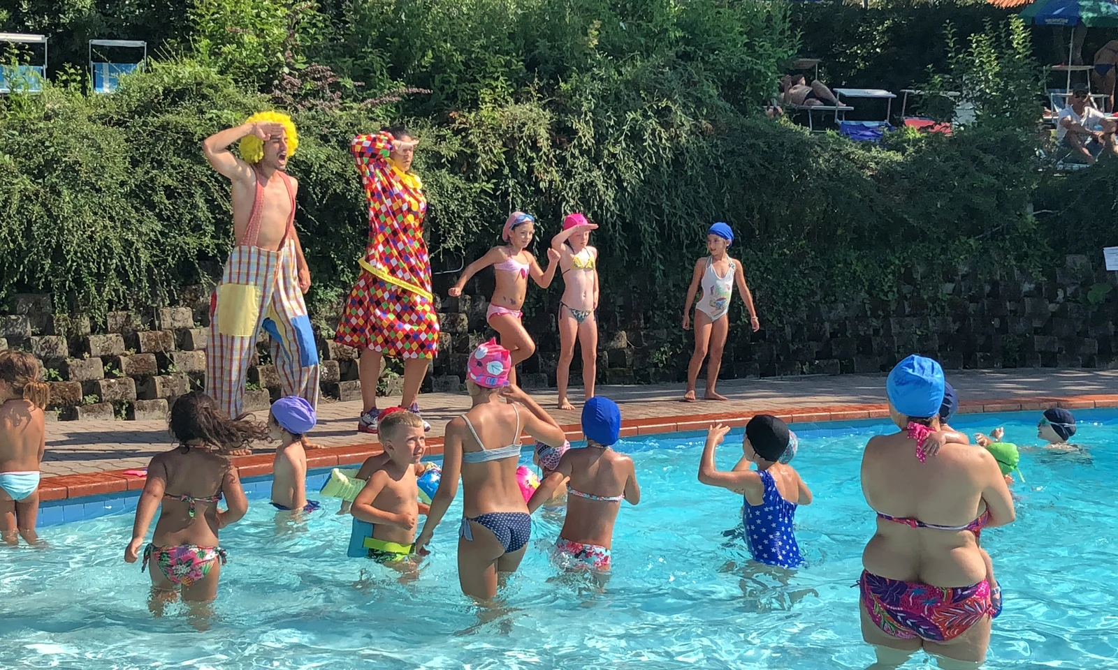 Children playing in a swimming pool, guided by two clowns in colorful costumes at Centro Vacanze San Marino