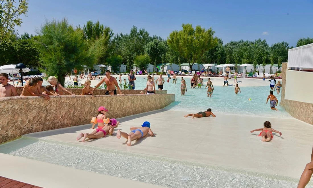 Children and adults playing in a crowded pool area surrounded by trees and white cabanas at Isamar